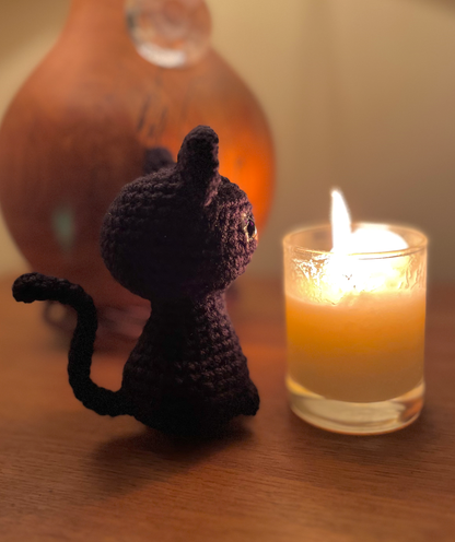 Mini crochet black cat displayed on a desk with witchy Halloween decor and spell books